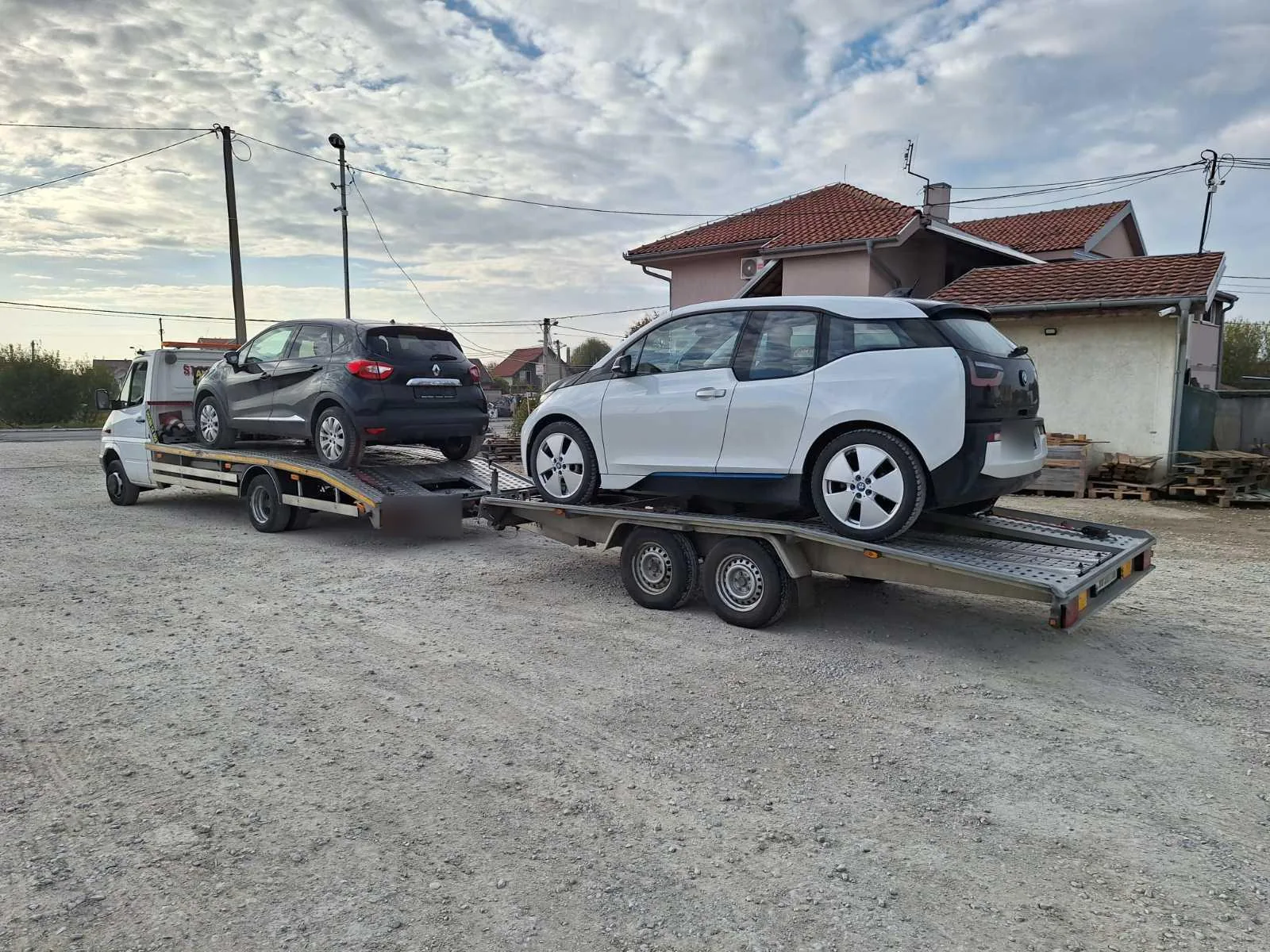 Dva automobila na šlep vozilu i prikolici, fotografisana sa zadnje bočne strane.