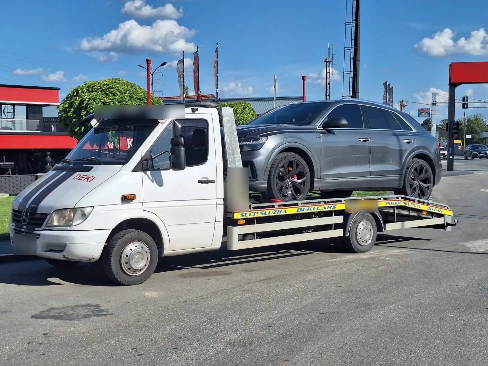 Sivi SUV na platformi šlep vozila Deki Team po sunčanom danu.
